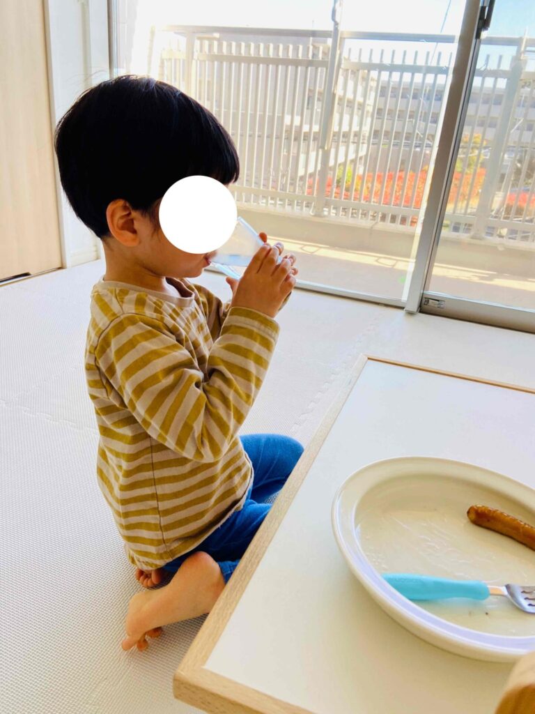 コップで牛乳を飲む子供、テーブルの上にはユニバーサル食器が置いてある